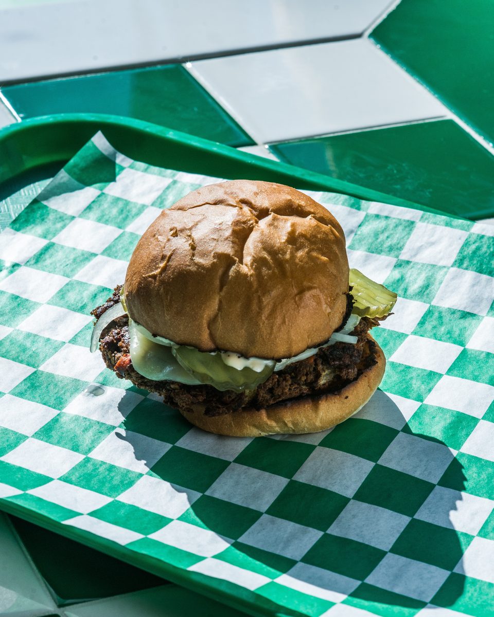 A cheeseburger with pickles and onions on a green and white checkered paper liner.