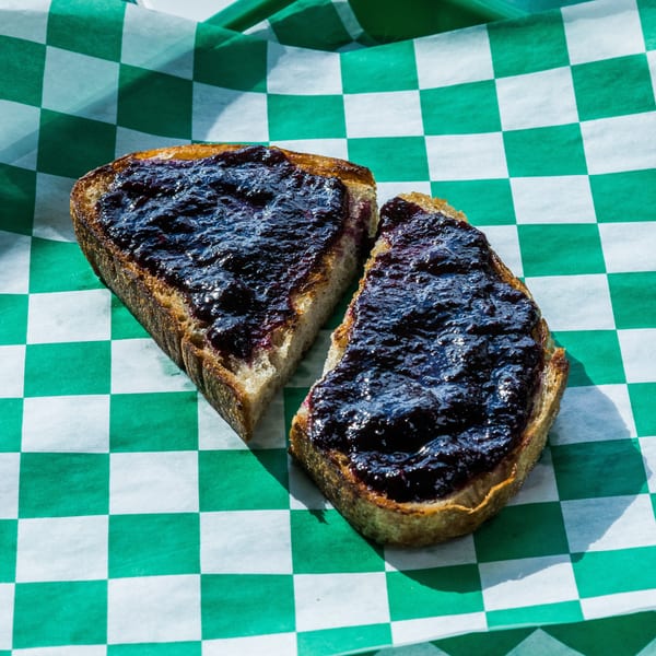 Two slices of toast with dark berry jam on green and white checkered paper.