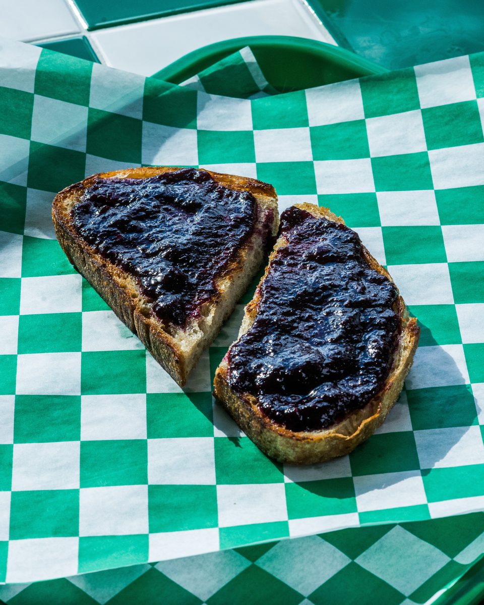 Two slices of toast with dark berry jam on green and white checkered paper.