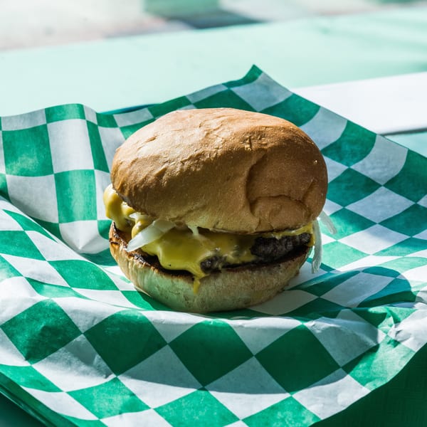 A cheeseburger with melted cheese and onions on a green and white checkered paper liner.