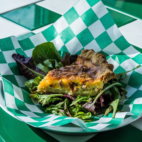 A slice of quiche with a side salad, served on green and white checkered paper.