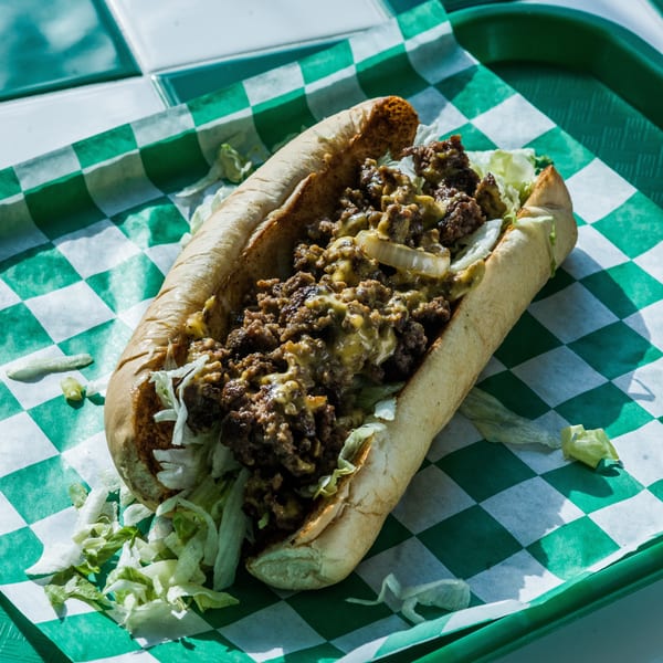 Cheesesteak sandwich with chopped meat, melted cheese, onions, and lettuce on a green checkered tray.