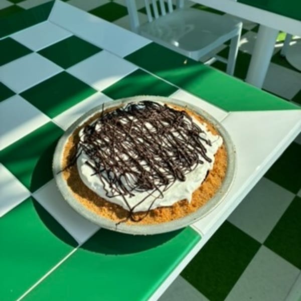 A chocolate drizzled pie with whipped cream on a green and white checkered table.